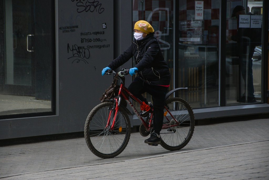 Женщина в маске и перчатках едет на велосипеде
