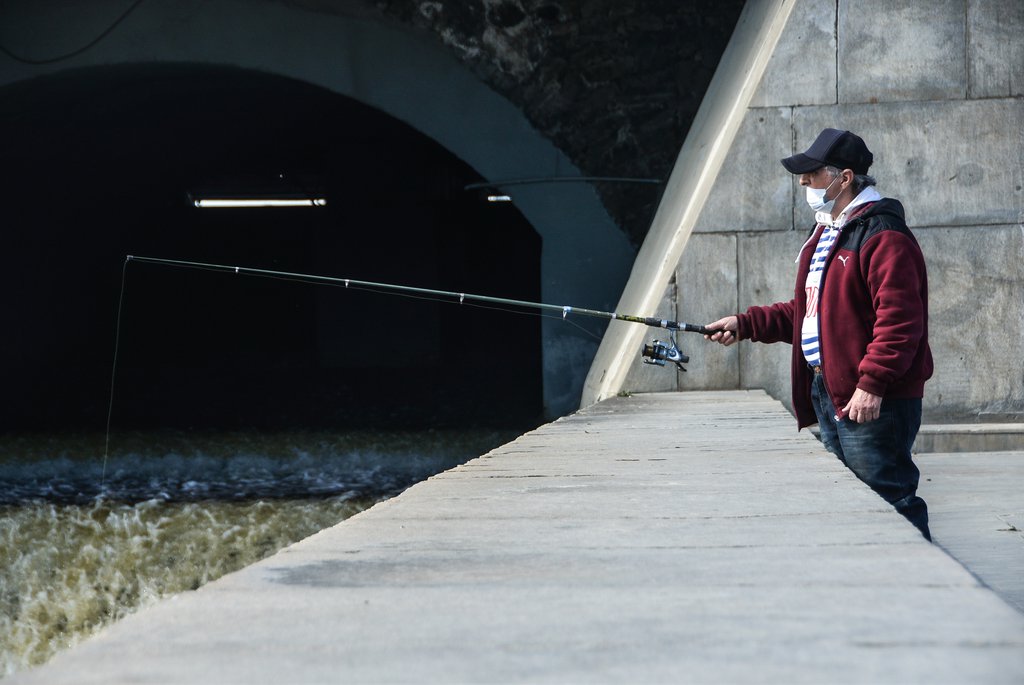 Мужчина в маске рыбачит на плотинке