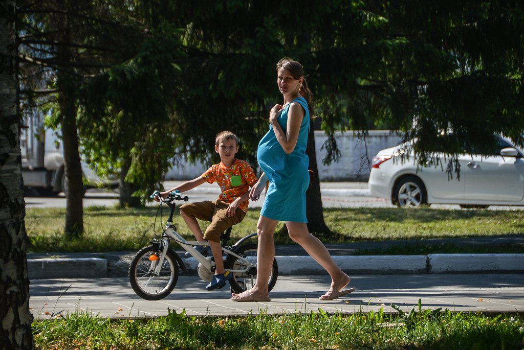 Беременная женщина идёт по улицу в жару с ребёнком