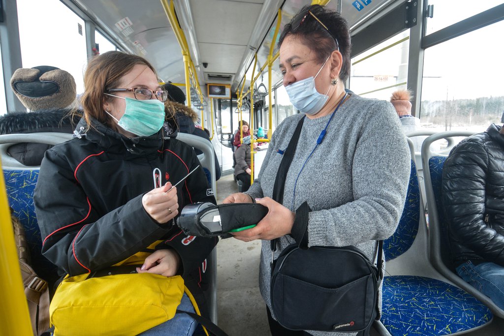 Девушка в маске в автобусе оплачивает билет