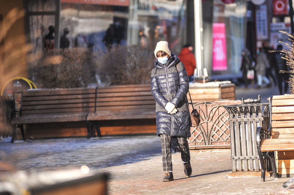 Женщина в маске идёт по улице зимой
