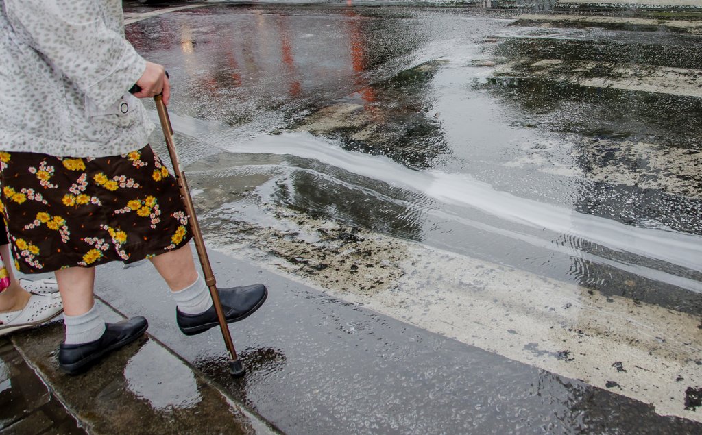 Пенсионерка переходит дорогу в дождь
